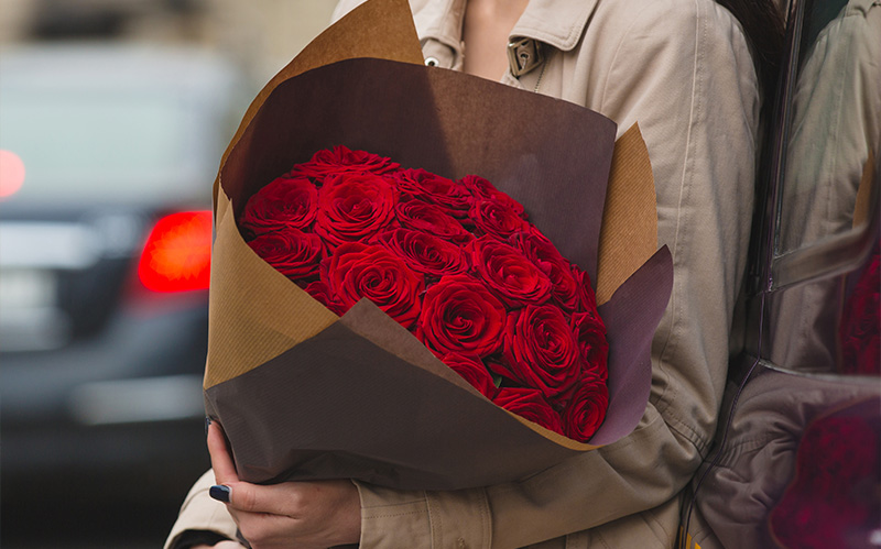 woman-holding-a-large-bouquet-of-vibrant-red-roses-wrapped-in-craft-paper